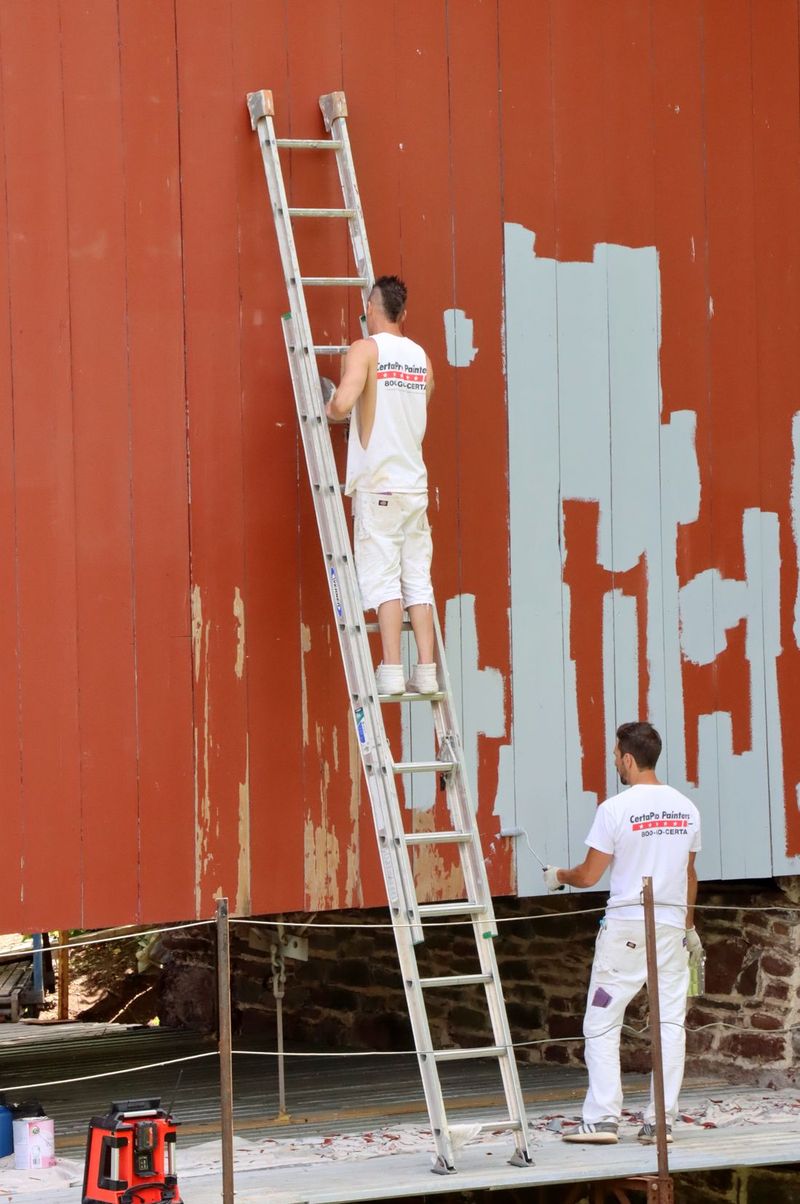 Painter coating the exterior wall of a home